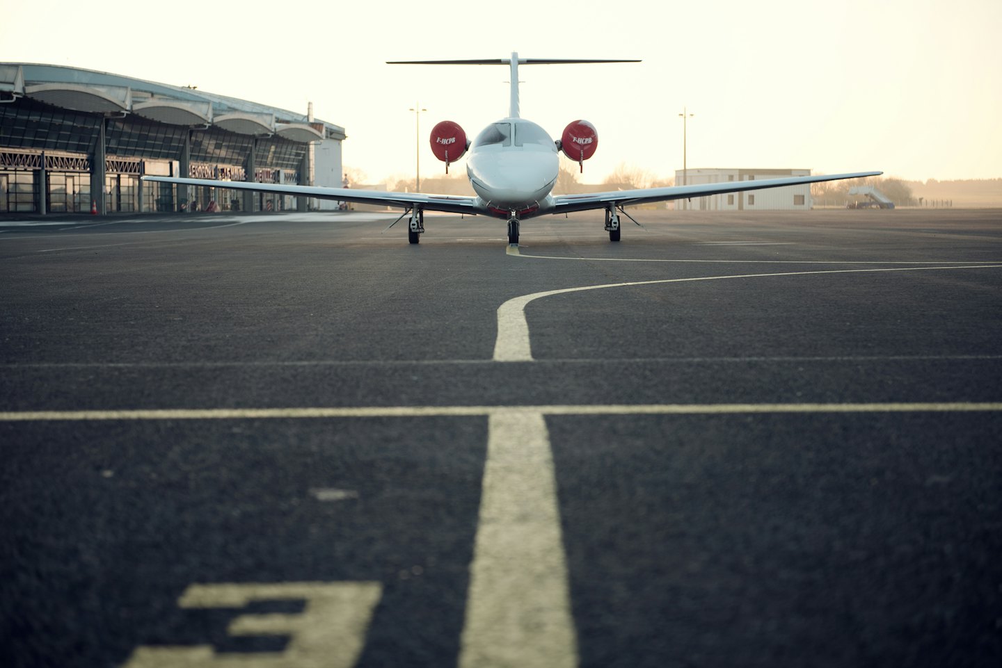 Ein schicker weißer Privatjet parkt im Morgengrauen auf einem Flughafenvorfeld.